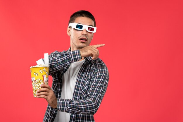 Front view young male holding popcorn package on light-red wall male movie theater cinema film fun times