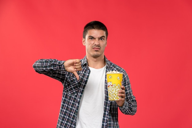 Вид спереди молодой мужчина держит пакет попкорна на светло-красной стене мужской кинотеатр кинотеатр фильм веселые времена