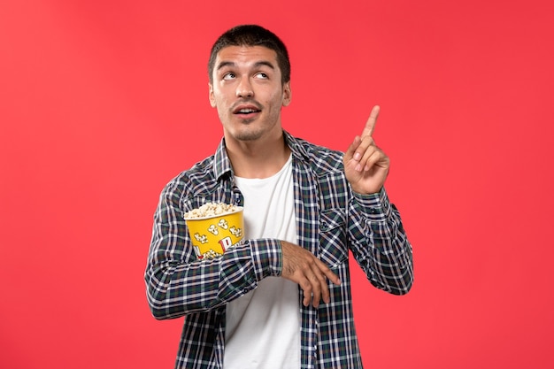 Вид спереди молодой мужчина держит пакет попкорна и позирует на светло-красной стене кинотеатр кино театр фильм мужчина мальчик