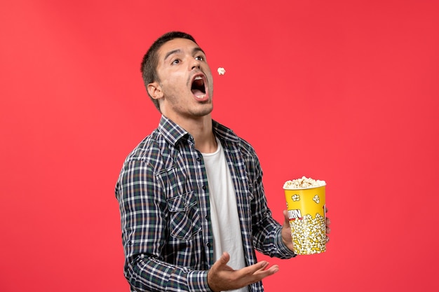 Вид спереди молодой мужчина, держащий пакет попкорна на красном полу кинотеатр, фильм, фильм