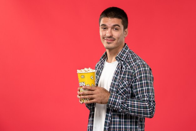 Front view young male holding popcorn package on the red surface cinema theater film movies