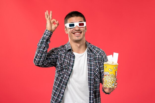 ポップコーンパッケージと赤い表面の映画館の映画館の映画のチケットを保持している正面図若い男性