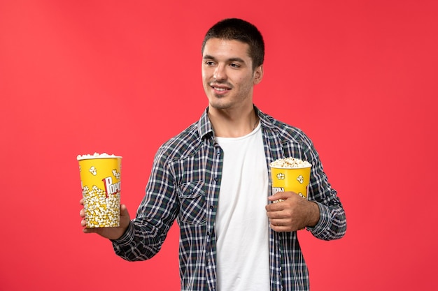 Вид спереди молодой мужчина с пакетами попкорна на светло-красной стене кинотеатр кинотеатр фильм мужчина