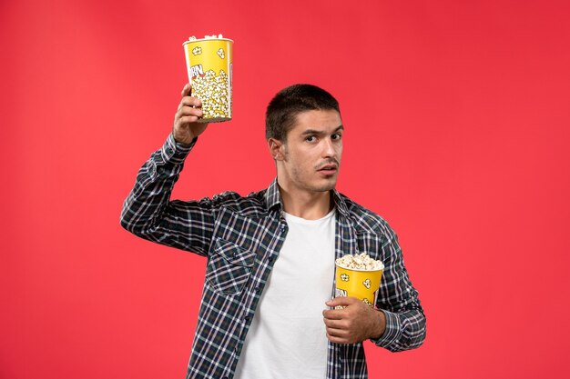 明るい赤の壁の映画館の映画館の映画館でポップコーンパッケージを保持している正面図若い男性