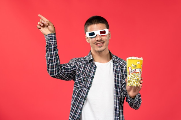 Вид спереди молодой мужчина держит попкорн в солнцезащитных очках на красной стене кино, кинотеатра, фильма
