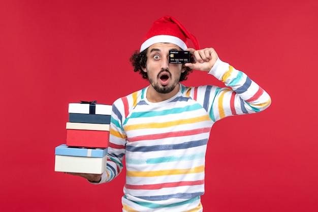 Front view young male holding presents and bank card on red desk new year money red