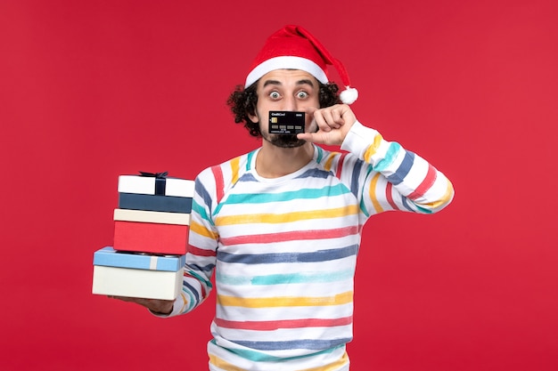 Front view young male holding presents and bank card on red floor new year money red