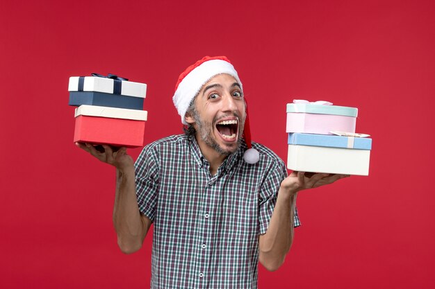 Front view young male holding presents on red desk