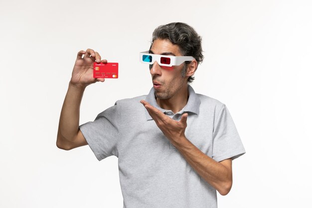 Front view young male holding red bank card in d sunglasses on a white surface