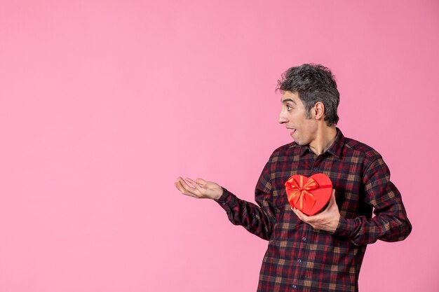 Front view young male holding red heart shaped present on pink wall