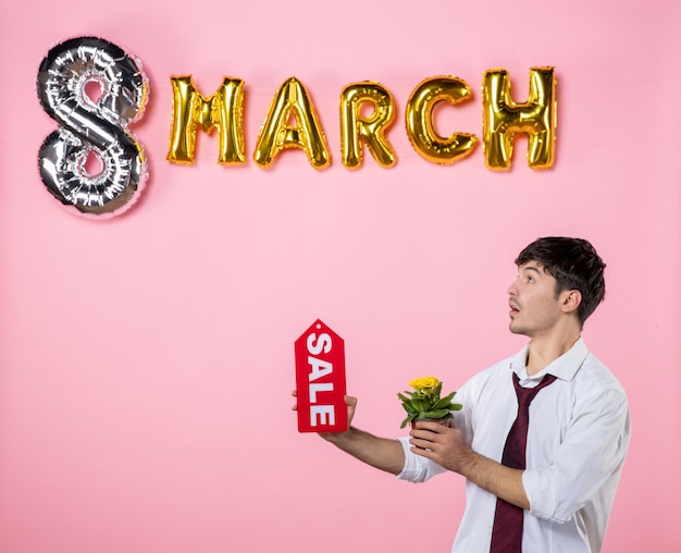 ピンク​の​背景色​の​3​月​の​装飾​が​付いている​赤い​販売​ネーム​プレート​を​保持している​正面図​若い​男性​お金​の​買い物​男性​女性​の​日​平等​フェミニン​な​パーティー​の​休日
