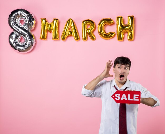 Front view young male holding red sale nameplate with march decoration on pink background color feminine shopping holiday equality money man present