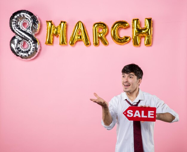 Front view young male holding red sale nameplate with march decoration on pink background color holiday party feminine shopping equality money present