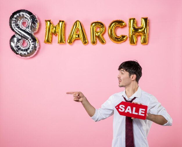 Front view young male holding red sale nameplate with march decoration on pink background color party feminine shopping equality money man present