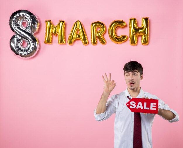 Front view young male holding red sale nameplate with march decoration on pink background color party feminine shopping holidays equality money man present