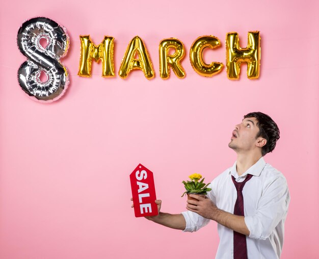 Front view young male holding red sale nameplate with march decoration on pink background money holiday womens day equality man feminine color party