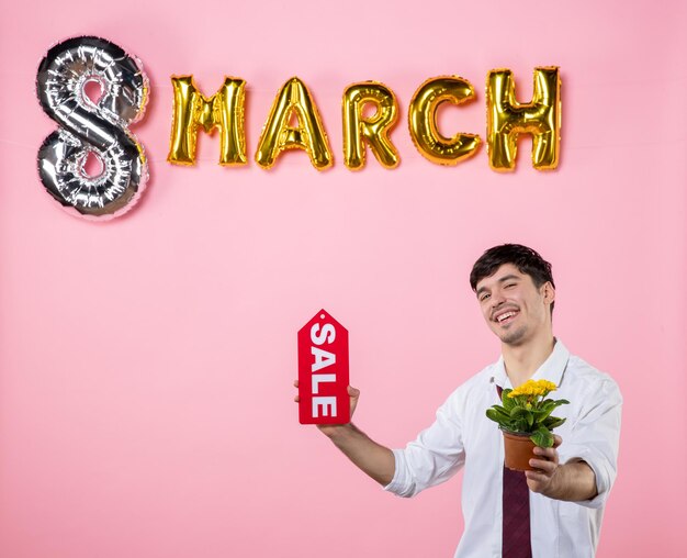 Вид спереди молодой мужчина держит красную табличку с мартовским украшением на розовом фоне деньги мужчина женский день равенство женская вечеринка праздничный цвет