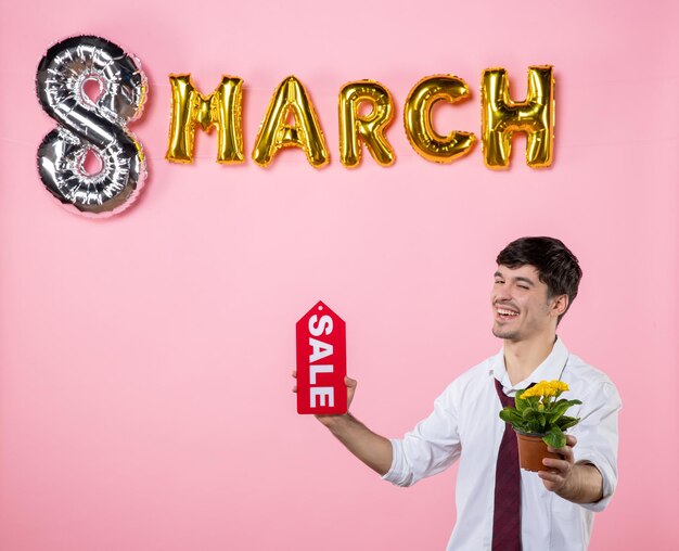 Front view young male holding red sale nameplate with march decoration on pink background money shopping womens day equality feminine party holiday color