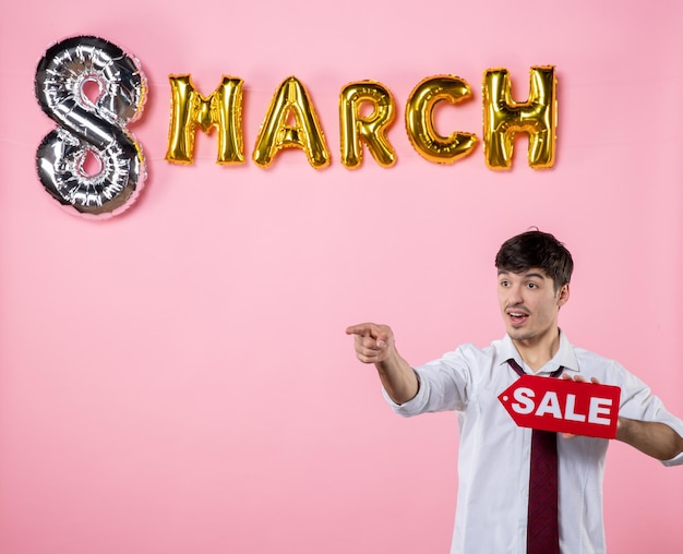 Front view young male holding red sale nameplate with march decoration on pink background party feminine shopping present color equality money man