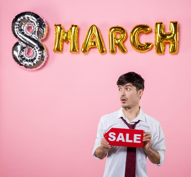 Front view young male holding red sale nameplate with march decoration on pink background shopping holiday color man womens day money feminine party equality