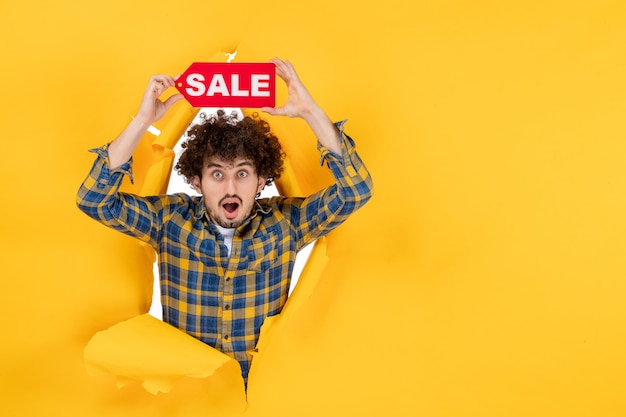 Бесплатное фото Вид спереди молодой мужчина держит красную распродажу на желтом разорванном фоне