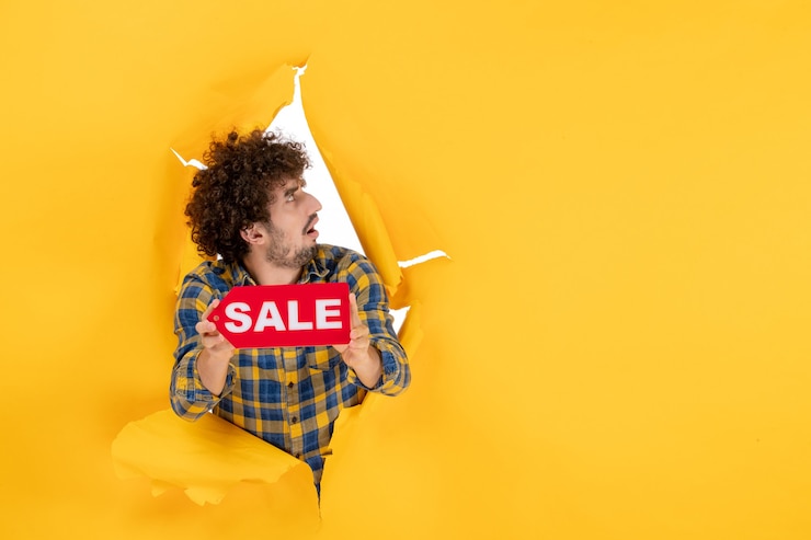Free Photo front view young male holding red sale writing on yellow ripped background