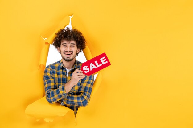 Free photo front view young male holding red sale writing on yellow ripped background