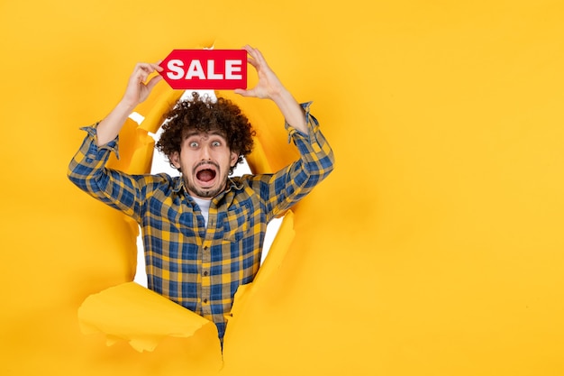 Front view young male holding red sale writing on yellow ripped background