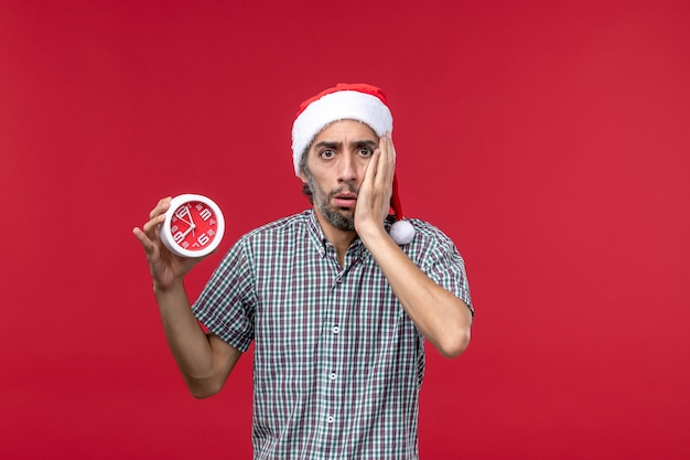 Вид спереди молодой мужчина держит круглые часы на красном фоне