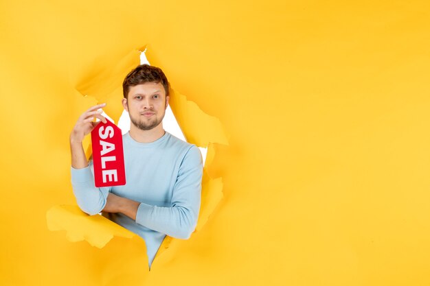 Front view young male holding sale writing on yellow ripped wall