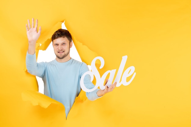 Free photo front view young male holding sale writing on yellow wall