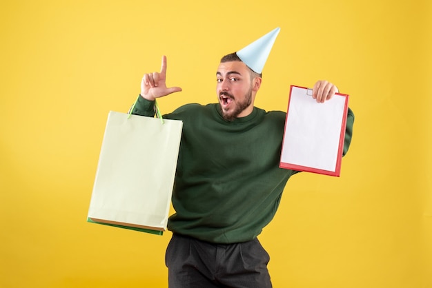 Front view young male holding shopping packages and note on yellow background