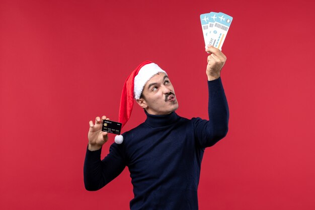 Вид спереди молодой мужчина держит билеты банковской карты на красном фоне