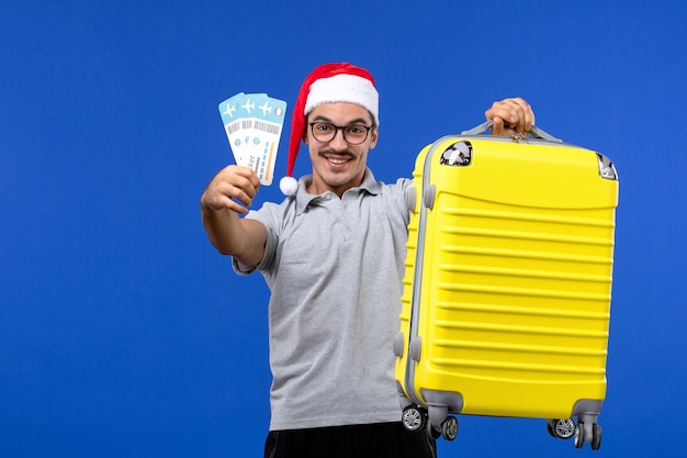 Front view young male holding tickets and heavy bag on a blue background flight vacation plane