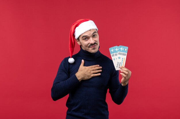 Front view young male holding two plane tickets on red background