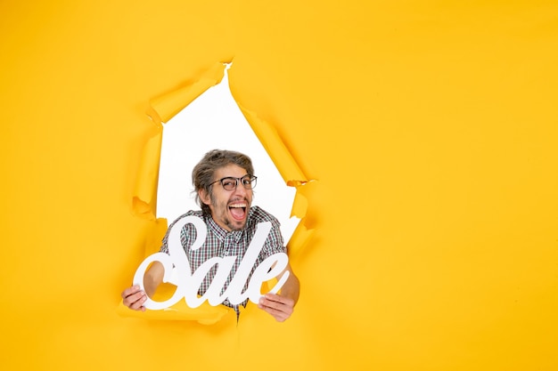 Free photo front view of young male holding white sale writing on yellow wall
