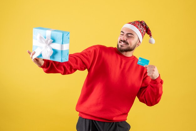 Front view young male holding xmas present and bank card on yellow desk