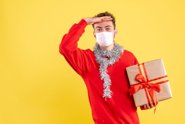 Front view young male holding xmas present in sterile mask looking