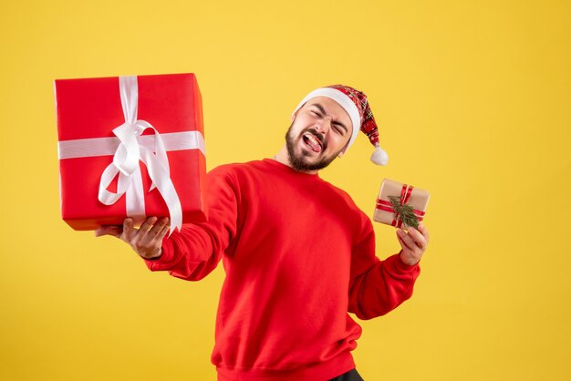 Вид спереди молодой мужчина держит рождественские подарки на желтом фоне