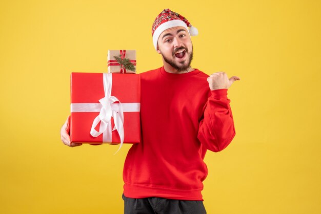 Вид спереди молодой мужчина держит рождественские подарки на желтом фоне