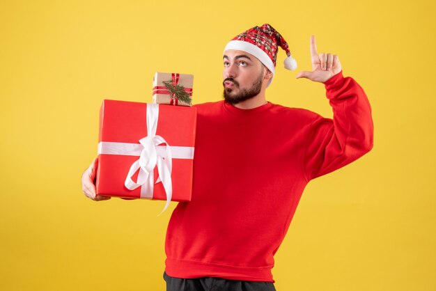 黄色の背景にクリスマスプレゼントを保持している正面図若い男性