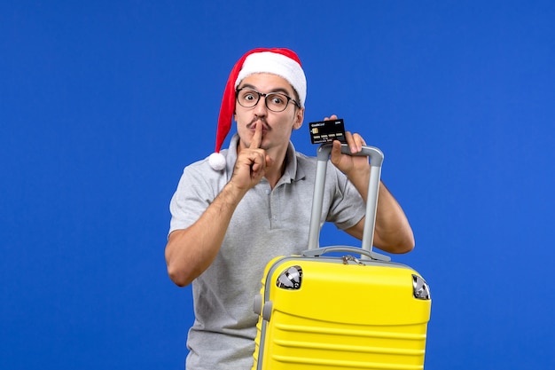 Front view young male holding yellow bag bank card on a blue desk vacation trip emotions