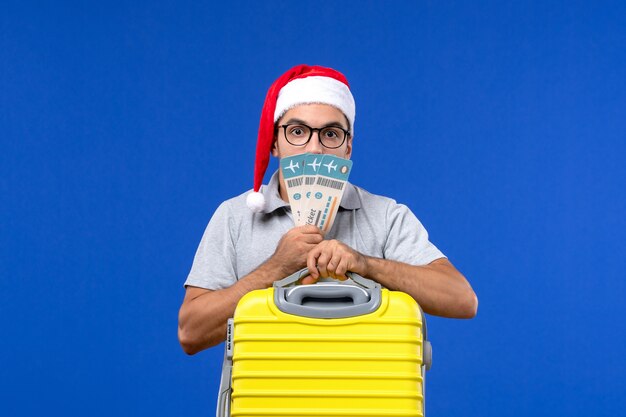 Front view young male holding yellow bag and tickets on blue background flight vacation plane