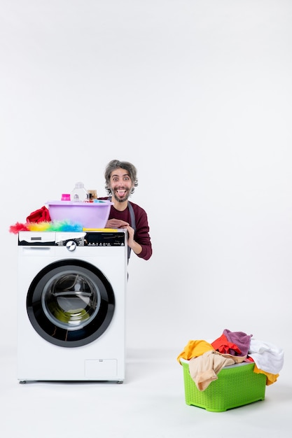 Free photo front view young male housekeeper in apron sitting behind washer laundry basket on white wall