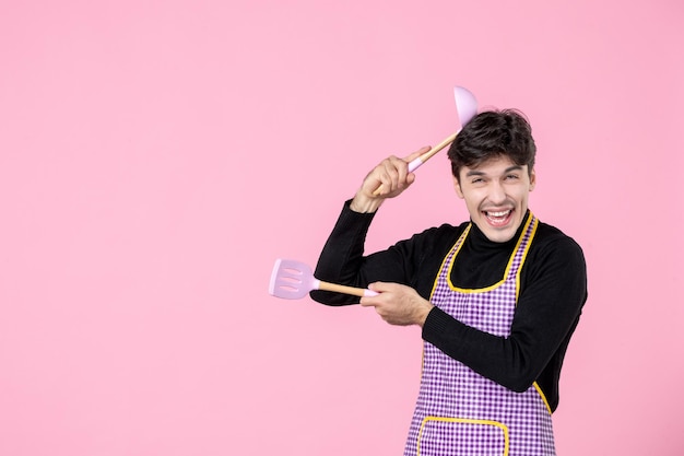 正面図ピンクの背景にスプーンを持っている岬の若い男性仕事生地職業料理人チーフカラー水平制服料理