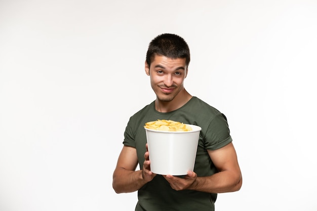 Вид спереди молодой мужчина в зеленой футболке, держащий картофельные чипсы на белом столе, человек одинокий фильм, кино