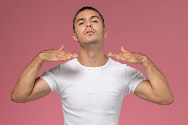 ピンクの背景に上げられた手でポーズをとって白いtシャツで正面の若い男性