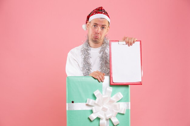 ピンクの背景にファイルノートを保持しているプレゼントの中の正面図若い男性