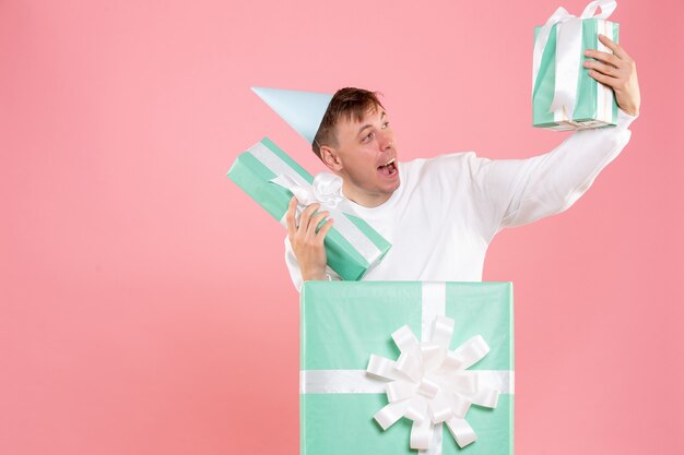 Front view young male inside present holding other presents on pink background