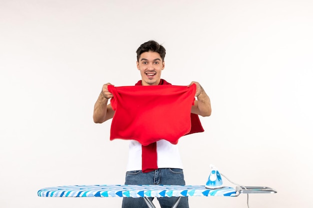 Front view young male behind ironing board folding towels on white